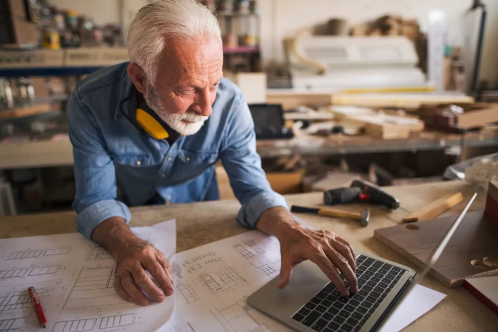 Älterer Handwerker schaut auf sein Laptop
