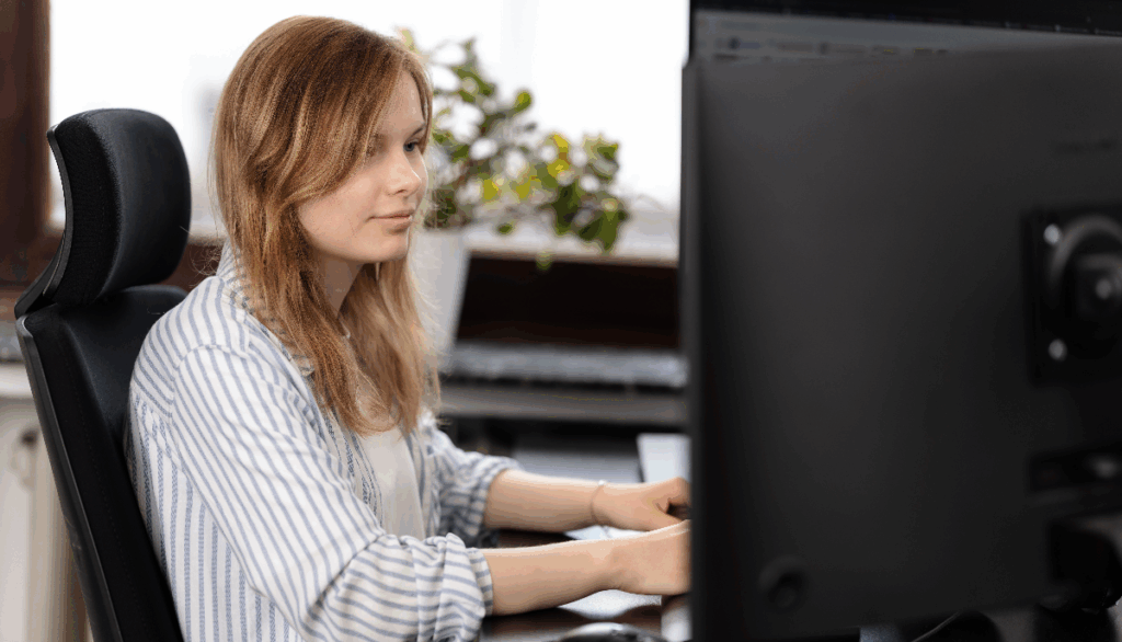 Mitarbeiterin Alicia von NEOVER arbeitet am Schreibtisch vor einem Monitor, freundliches Agenturbild im Büro